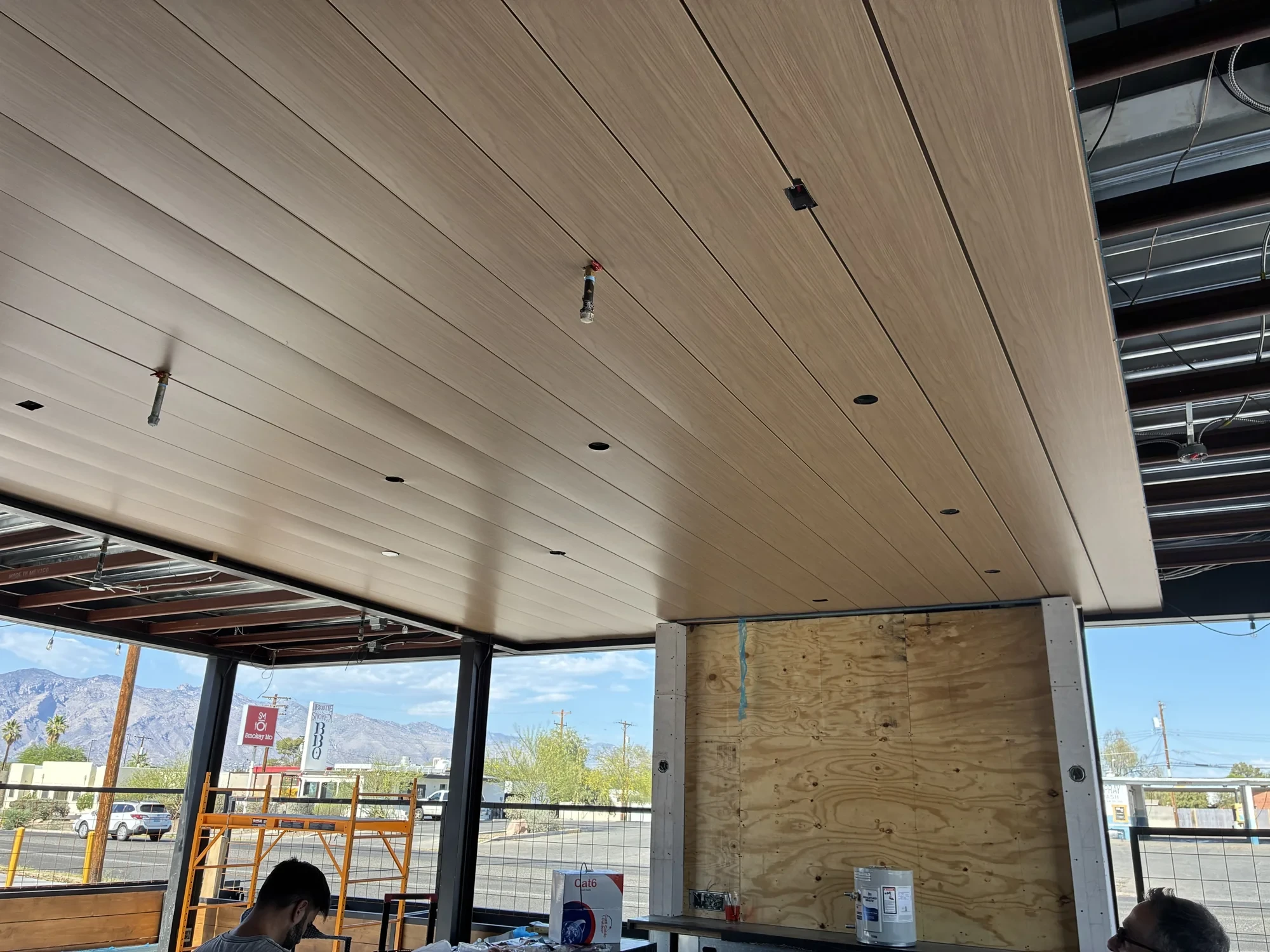 Real wood-grain metal ceiling with visible grain, panel joints, and light openings during installation
