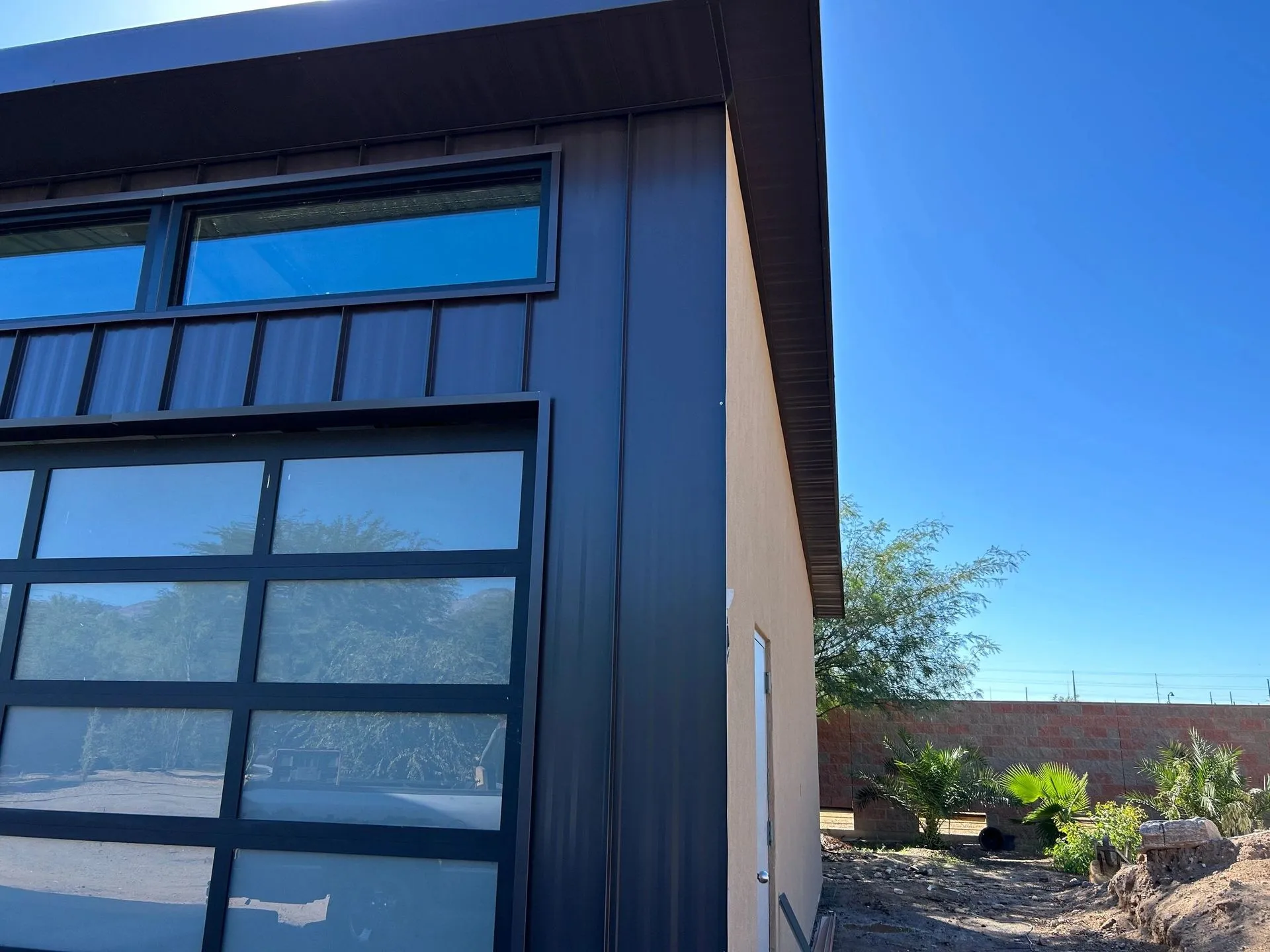 Modern Sonoran desert home with charcoal vertical standing-seam wall panels and glass garage door