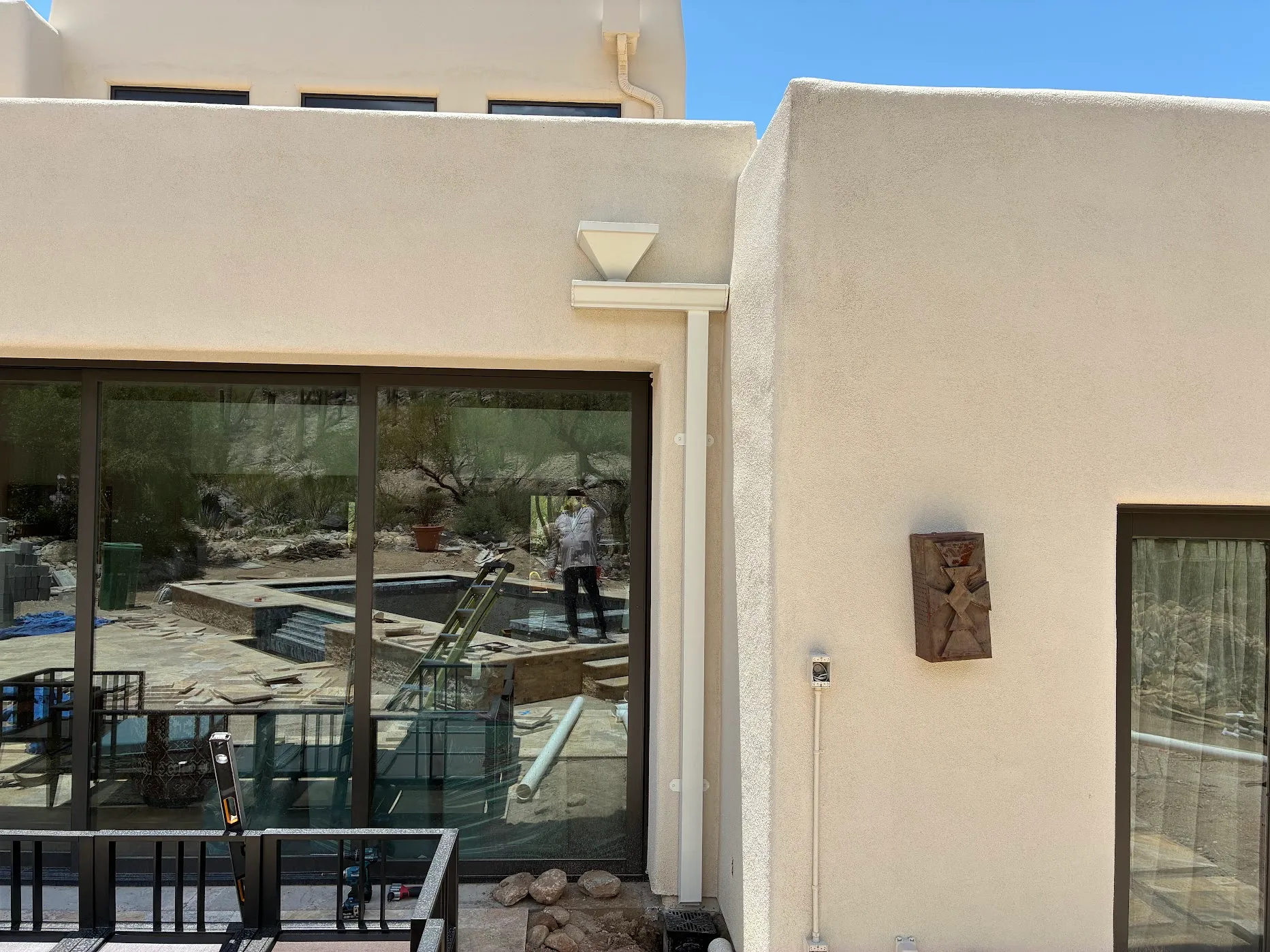 Tan seamless gutter color-matched to a stucco parapet, downspout running the full elevation to grade