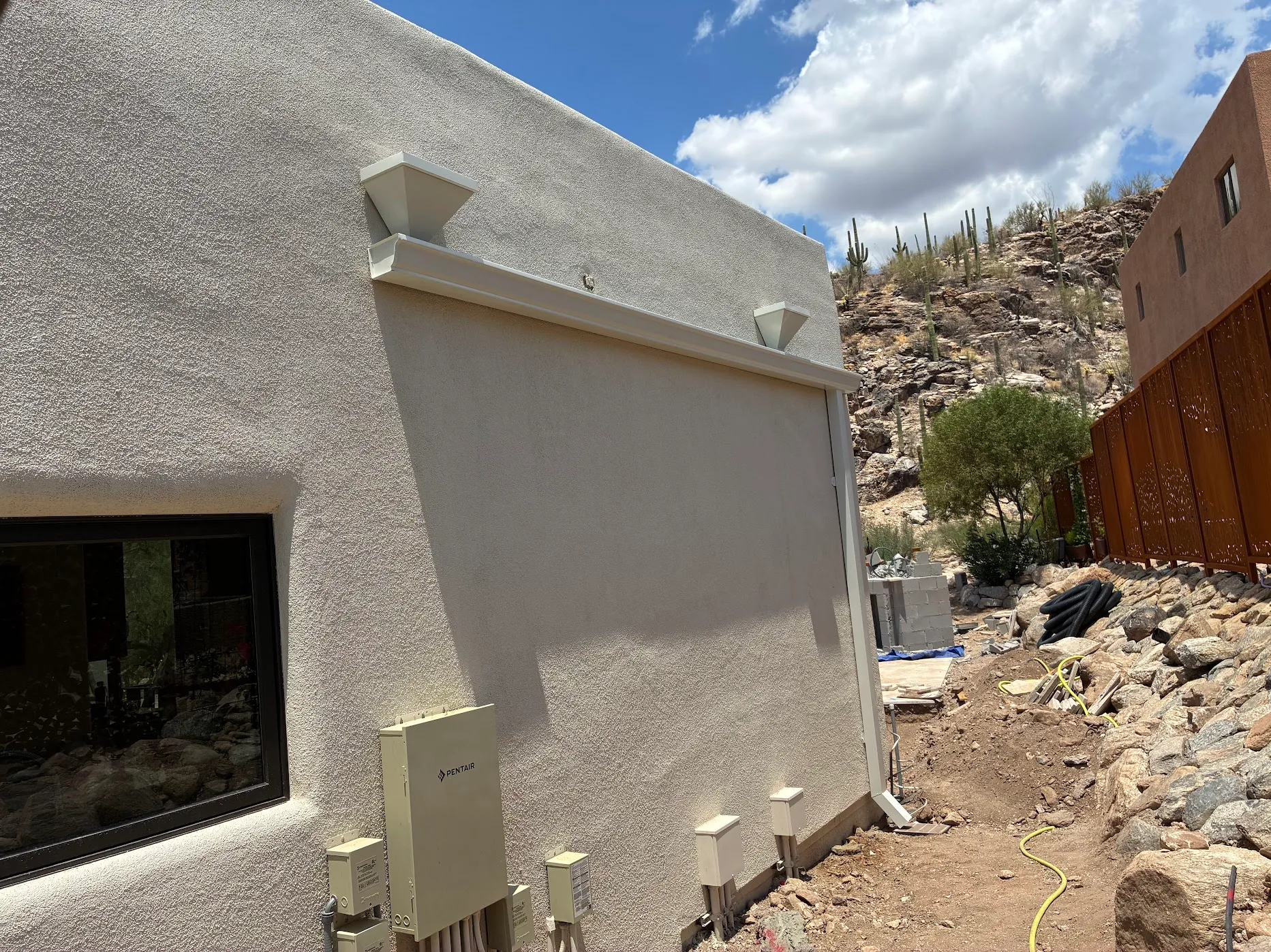 Tan seamless gutter at the top of a stucco parapet wall, downspout returning down the side elevation