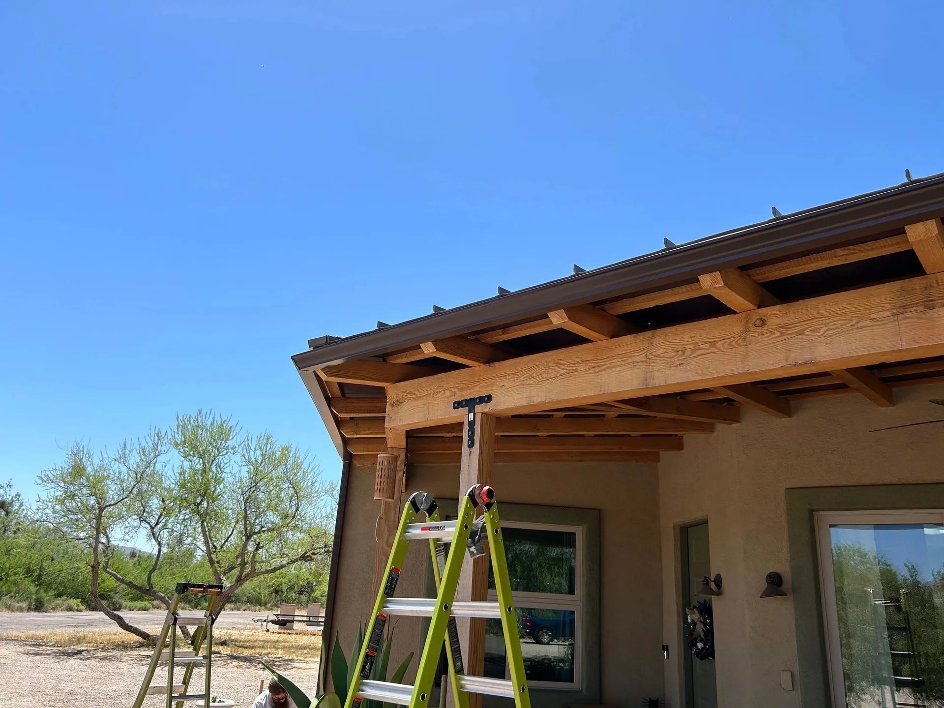 Wood-grain printed metal patio cover install in progress on a Tucson home, panels going up over fresh framing