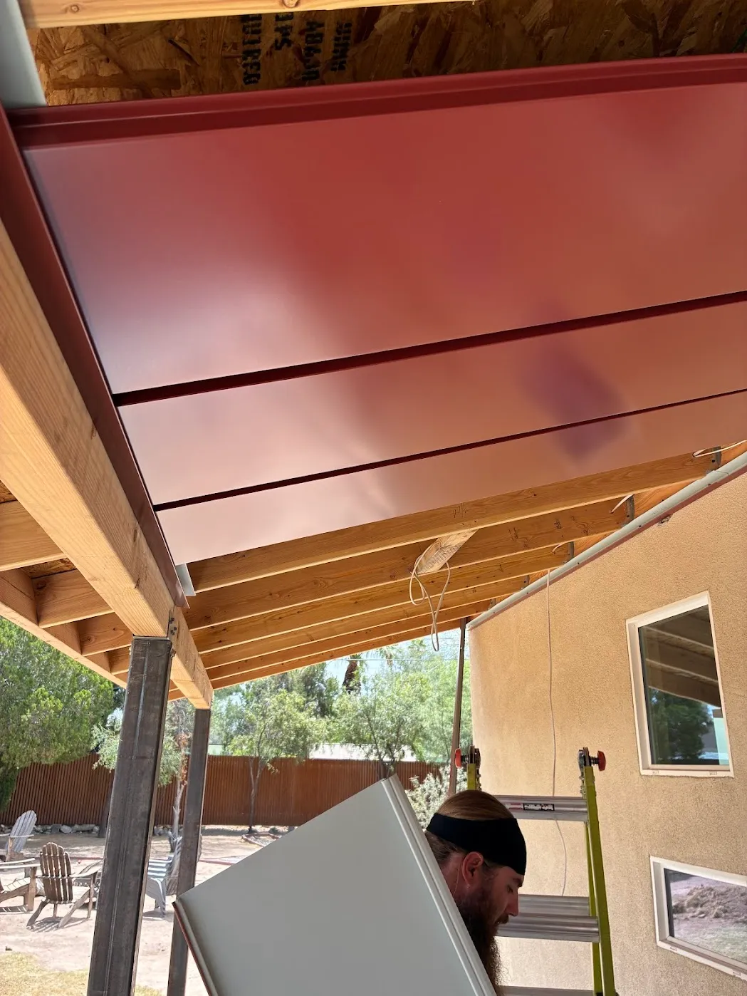 Red standing seam patio panels mid-install over wood framing