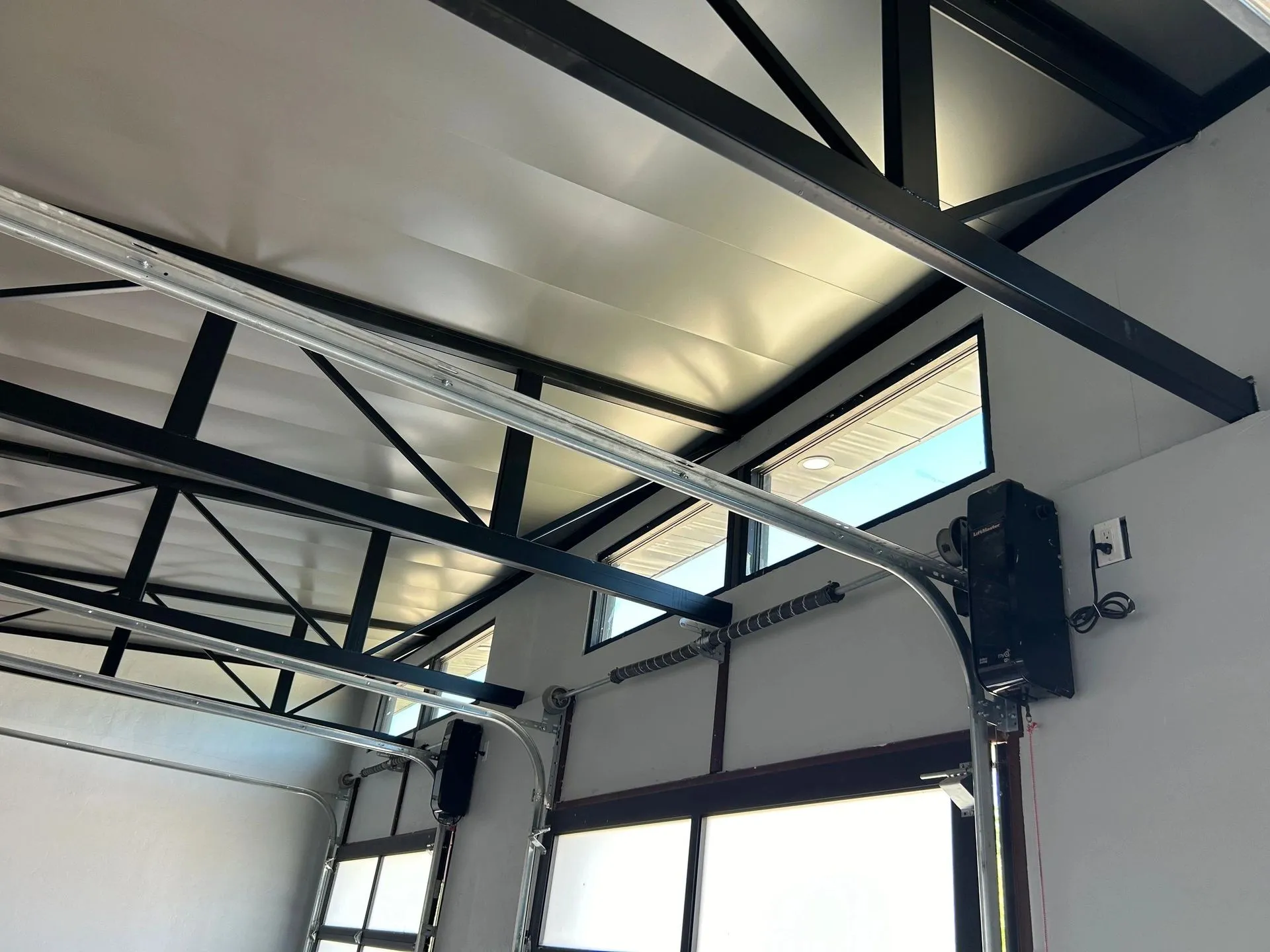 Garage-door bay inside a shop with black trusses, white under-decking, and overhead door tracks