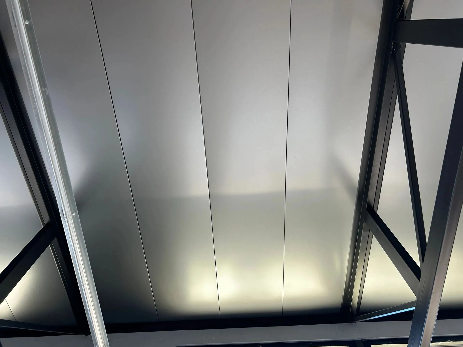 Tight detail of metal under-decking panels on black trusses inside a finished shop