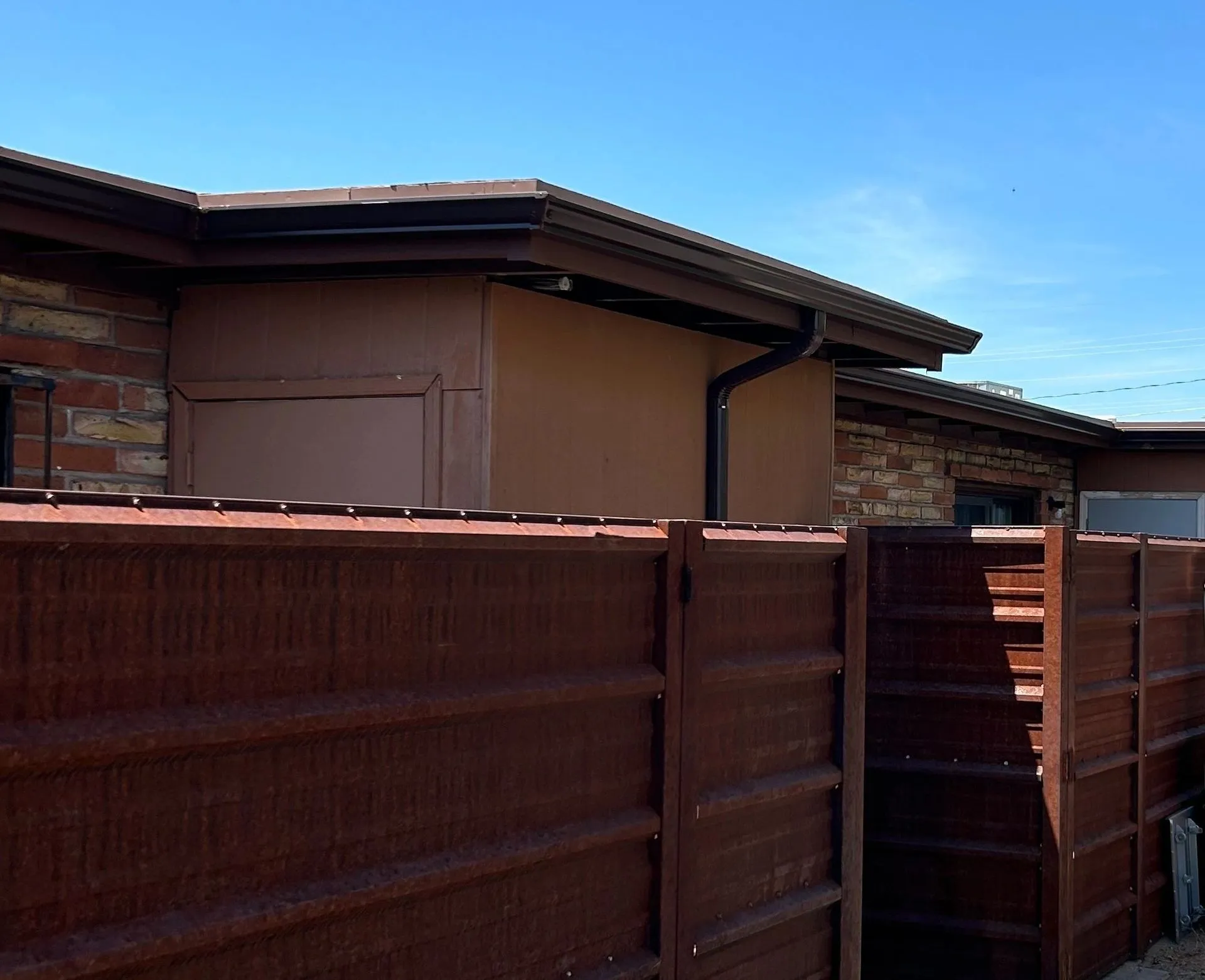 Brown K-style seamless gutter and downspout against a corten steel fence on a Tucson home