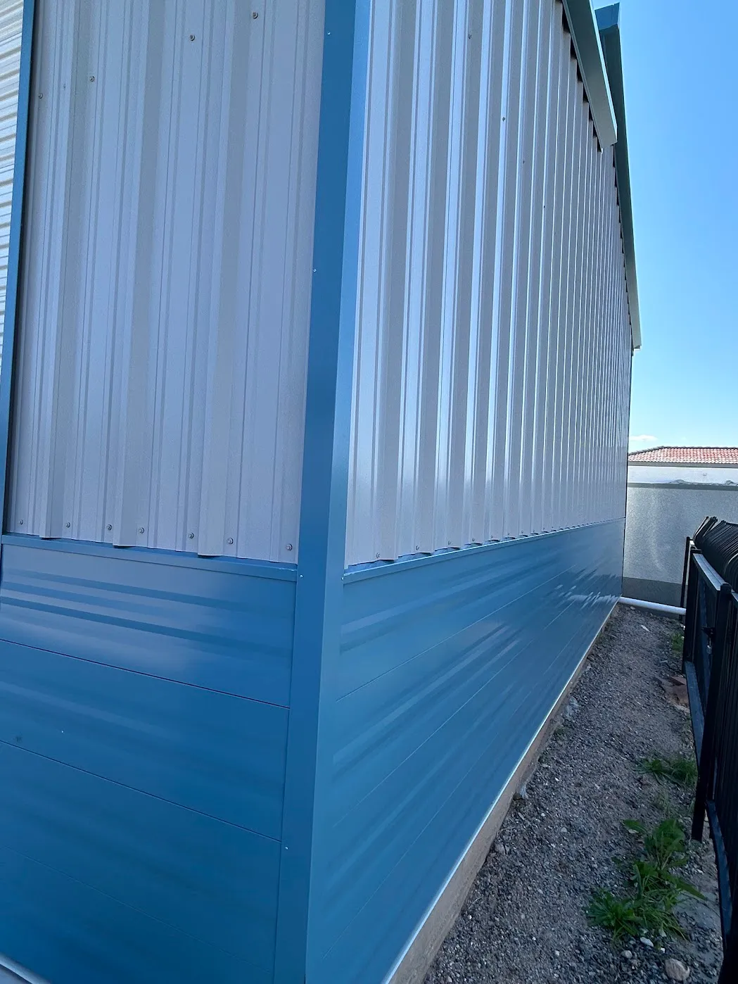 Two-tone metal wall: white R-panel upper section over slate-blue horizontal-profile wainscot, side elevation