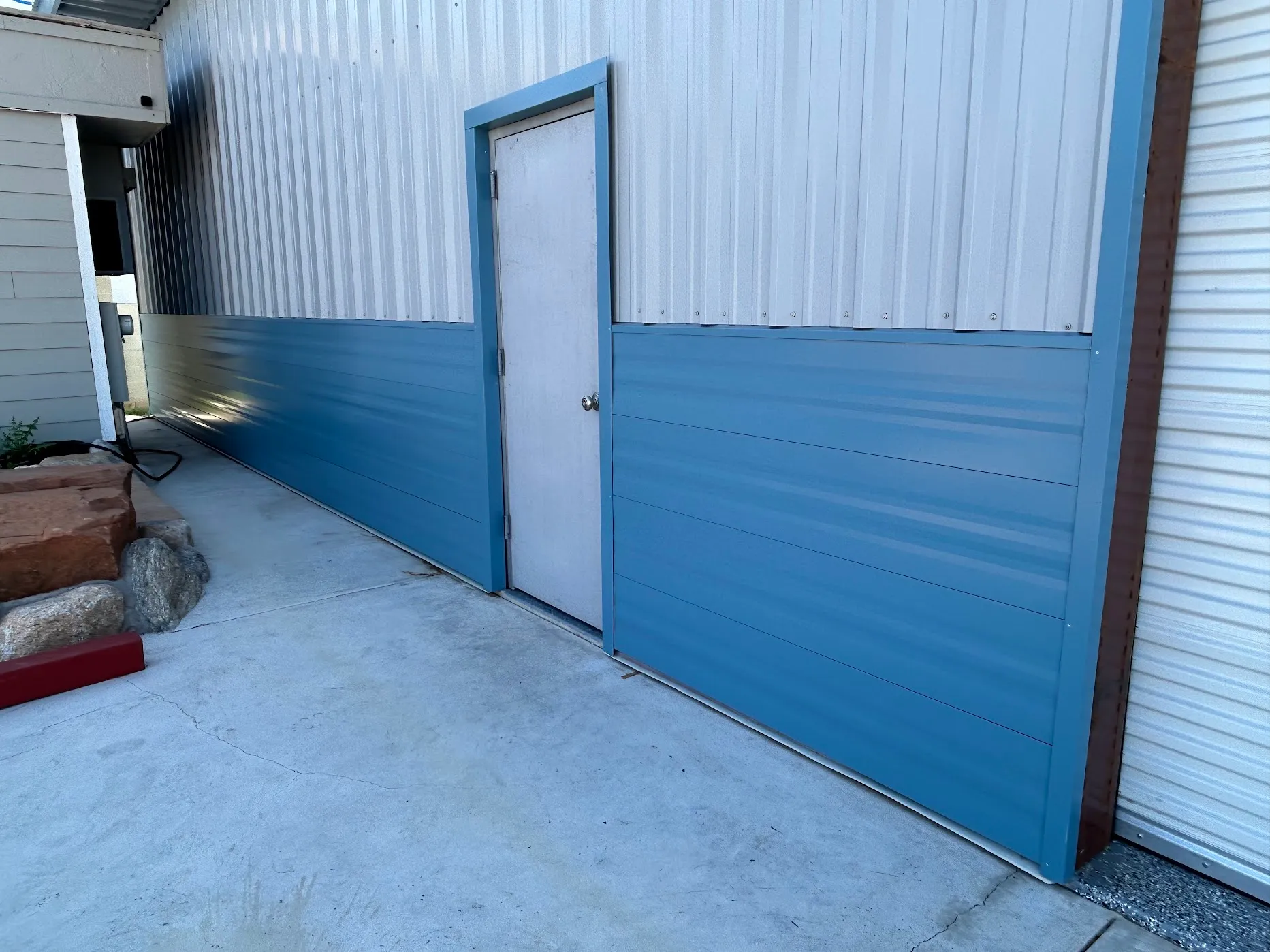 White R-panel upper wall with slate-blue horizontal-profile wainscot wrapping a metal access door, full elevation